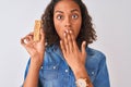 Young brazilian woman eating granola bar standing over isolated white background cover mouth with hand shocked with shame for Royalty Free Stock Photo