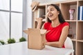 Young brazilian woman looking inside cardboard box pointing thumb up to the side smiling happy with open mouth Royalty Free Stock Photo