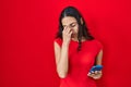 Young brazilian woman using smartphone over red background tired rubbing nose and eyes feeling fatigue and headache Royalty Free Stock Photo