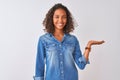 Young brazilian woman wearing denim shirt standing over isolated white background smiling cheerful presenting and pointing with