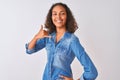 Young brazilian woman wearing denim shirt standing over isolated white background smiling doing phone gesture with hand and Royalty Free Stock Photo