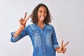 Young brazilian woman wearing denim shirt standing over isolated white background smiling with tongue out showing fingers of both Royalty Free Stock Photo