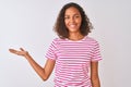 Young brazilian woman wearing pink striped t-shirt standing over isolated white background smiling cheerful presenting and