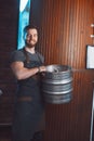 A young brewer in an apron holds a barrel with beer in the hands