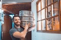 A young brewer in an apron holds a barrel with beer in the hands