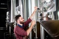 Young brewer wearing a leather apron is testing beer at a modern brewery