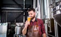 Young brewer wearing a leather apron is testing beer at a modern brewery