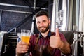 Young brewer wearing a leather apron is testing beer at a modern brewery