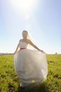 Young bride in long white dress walking on green field Royalty Free Stock Photo