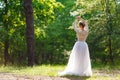 A young bride stands in the park with her back. Pretty unusually posing on camera