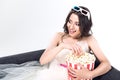 young bride in wedding dress and 3d goggles holding bucket of popcorn and sitting on couch