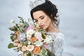 Young bride with wedding hairstyle and luxury diadem holding a big luxury bouquet of exotic flowers in her hands