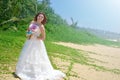 A young bride in a white airy dress is standing with a bouquet of lotuses. girl smiling on a tropical beach on the island Royalty Free Stock Photo