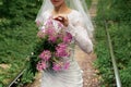 Bride in a white wedding dress and veil, holds in her hands, examines and touches a chic bouquet of purple wildflowers Royalty Free Stock Photo