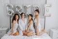 Young bridesmaids in white silk dresses on a bed in the bride's room. Royalty Free Stock Photo