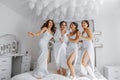 Young bridesmaids in white silk dresses on a bed in the bride's room. Royalty Free Stock Photo