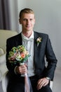 Young broom in a dark suit and a wedding bouquet smiling for a photo