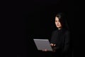 A young brown-haired woman in black clothes with a covered head with a laptop in her hands. on a black isolated background Royalty Free Stock Photo