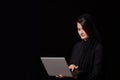 A young brown-haired woman in black clothes with a covered head with a laptop in her hands. on a black isolated background Royalty Free Stock Photo