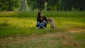 A young brownhair woman in a park communicates with her outbred dog.