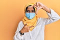 Young brunette arab woman wearing traditional islamic hijab and medical mask smiling making frame with hands and fingers with Royalty Free Stock Photo