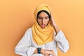 Young brunette arab woman wearing traditional islamic hijab scarf looking at the watch time worried, afraid of getting late Royalty Free Stock Photo