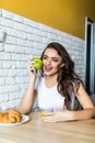 Young brunette attractive woman cooking in kitchen in morning, eating green apple, smiling, happy mood, positive housewife, health Royalty Free Stock Photo