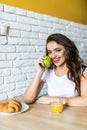 Young brunette attractive woman cooking in kitchen in morning, eating green apple, smiling, happy mood, positive housewife, health Royalty Free Stock Photo