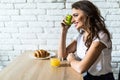 Young brunette attractive woman cooking in kitchen in morning, eating green apple, smiling, happy mood, positive housewife, health Royalty Free Stock Photo