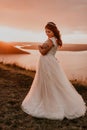 Bride in white wedding dress with a crown on her head stands on cliff against the background of the river and islands