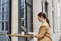 Young brunette businesswoman in beige formalwear using laptop in street cafe