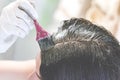 A young brunette caucasian woman dying her hair with a pink brush using white gloves at her home