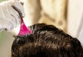 A young brunette caucasian woman dying her hair with a pink brush using white gloves at her home