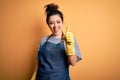 Young brunette cleaner woman wearing housekeeping gloves over yellow background doing happy thumbs up gesture with hand Royalty Free Stock Photo