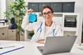 Young brunette doctor woman holding alarm clock looking positive and happy standing and smiling with a confident smile showing Royalty Free Stock Photo