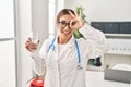 Young brunette doctor woman holding glass of water smiling happy doing ok sign with hand on eye looking through fingers Royalty Free Stock Photo