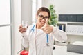 Young brunette doctor woman holding glass of water smiling happy and positive, thumb up doing excellent and approval sign Royalty Free Stock Photo