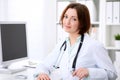 Young brunette female doctor sitting at a desk and working on the computer at the hospital office. Royalty Free Stock Photo