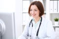 Young brunette female doctor sitting at a desk and working on the computer at the hospital office. Royalty Free Stock Photo