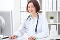 Young brunette female doctor sitting at a desk and working on the computer at the hospital office. Royalty Free Stock Photo