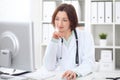 Young brunette female doctor sitting at a desk and working on the computer at the hospital office. Royalty Free Stock Photo