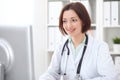 Young brunette female doctor sitting at a desk and working on the computer at the hospital office. Royalty Free Stock Photo