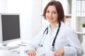 Young brunette female doctor sitting at a desk and working on the computer at the hospital office. Royalty Free Stock Photo