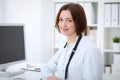 Young brunette female doctor sitting at the table and working with computer at hospital office Royalty Free Stock Photo