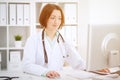 Young brunette female doctor sitting at the table and working with computer at hospital office Royalty Free Stock Photo