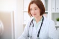 Young brunette female doctor sitting at the table and working with computer at hospital office Royalty Free Stock Photo