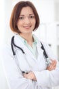 Young brunette female doctor standing with arms crossed and smiling at hospital. Royalty Free Stock Photo