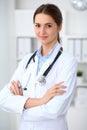 Young brunette female doctor standing with arms crossed and smiling at hospital. Physician ready to examine patient Royalty Free Stock Photo