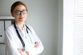 Young brunette female doctor standing with arms crossed and smiling at hospital. Physician ready to examine patient Royalty Free Stock Photo