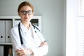 Young brunette female doctor standing with arms crossed and smiling at hospital. Physician ready to examine patient Royalty Free Stock Photo